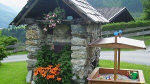 A rustic stone structure with a sloped roof, a wooden bench, and a small garden with flowers. - Stunning  villa for 5 people with WIFI, TV and balcony (Bruck An Der Großglocknerstraße)