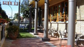 An outdoor patio area with brick flooring, metal chairs, and tables, surrounded by columns and a covered walkway. - Hotel La Rosa (Borgo San Lorenzo)