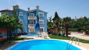 A hotel with a swimming pool, a blue exterior, and a balcony with a blue umbrella. - Cosy apartment for 5 people with A/C, pool, TV, terrace and pets allowed (Medulin)