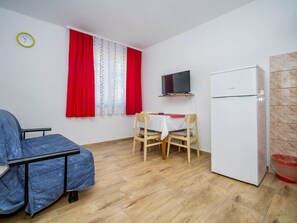 A small, well-lit room with a bed, a TV mounted on the wall, a dining table with chairs, and a white refrigerator. - Beautiful apartment for 3 guests with A/C, pool, TV, terrace and pets allowed (Medulin)