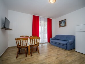 Um espaço de estar compacto com mesa e cadeiras, um sofá azul, uma geladeira branca e um quadro na parede.
