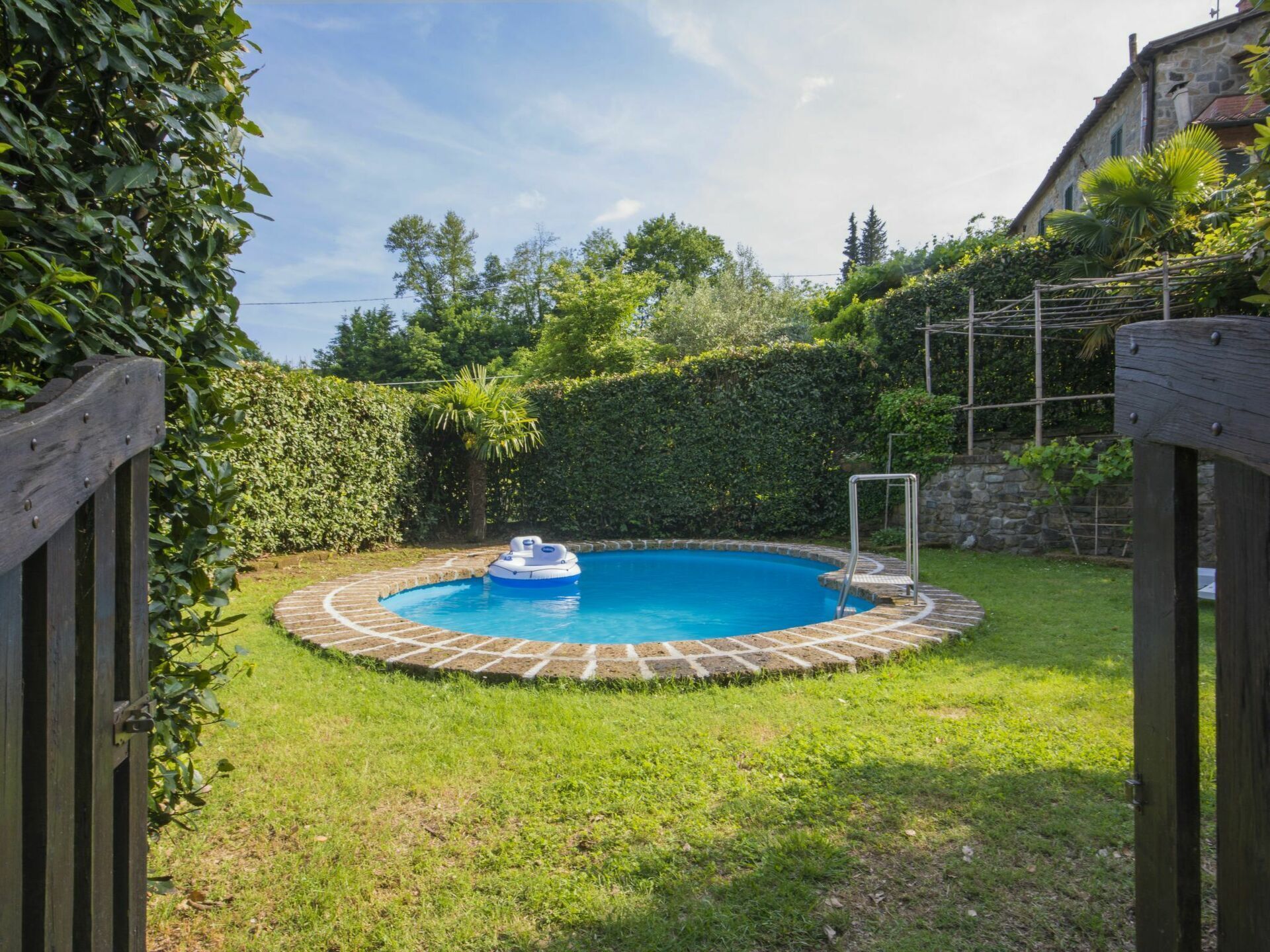 Una piscina circular con un muelle flotante, rodeada por un borde de ladrillo y una terraza de madera.