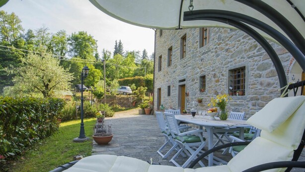 Un bâtiment en pierre doté d’un patio comprenant une table et des chaises, un fauteuil suspendu et un jardin avec un lampadaire.