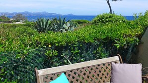 Une terrasse avec un banc en bois, une clôture en métal et une vue sur la mer et les montagnes.