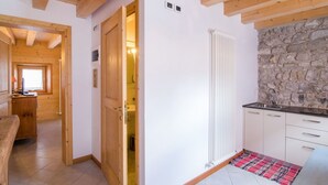 A wooden interior with a kitchen area, stone wall, and a door leading to a bathroom. - Cosy apartment for 2 guests with WIFI, TV, patio and pets allowed (Barcis)