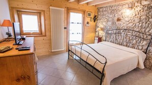 A bedroom with a stone wall, wooden ceiling beams, a bed with a metal frame, a bedside table with a lamp, and a window with blinds. - Cosy apartment for 2 guests with WIFI, TV, patio and pets allowed (Barcis)