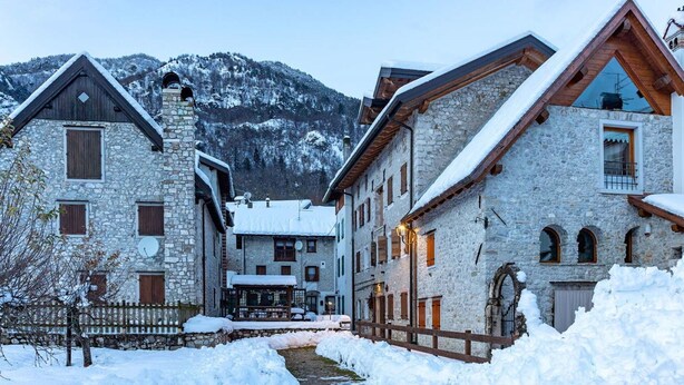 A snow-covered village with stone buildings, a wooden fence, and a mountain in the background. - Cosy apartment for 2 guests with WIFI, TV, patio and pets allowed (Barcis)