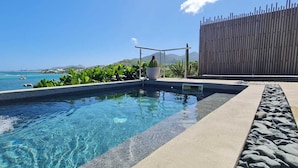 A clear pool with a waterfall feature, surrounded by tropical plants and a view of the sea. - VILLA PINEL BAY VIEW - Sea and St Barth view villa with pool and sea access (ST MARTIN)