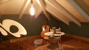 A cozy attic room with a sloped ceiling, a hanging light bulb, a guitar, a small table with a plant, and a chair. - VILLA PINEL BAY VIEW - Sea and St Barth view villa with pool and sea access (ST MARTIN)