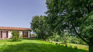 A house with a tiled roof, a well-maintained lawn, and a large tree in the foreground. - Nice apartment in villa for 2 guests with WIFI, A/C, pool, patio and panoramic view (Cinigiano)