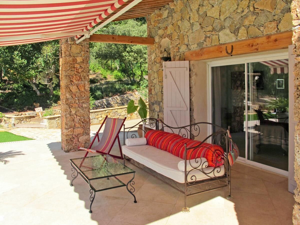 A stone building with a glass door, a covered patio with a striped awning, a cushioned bench, and a metal table.