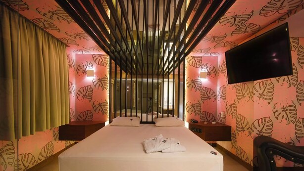 A hotel room with a large bed, a TV mounted on the wall, and a window with curtains. - Classe A Motel (São Paulo)
