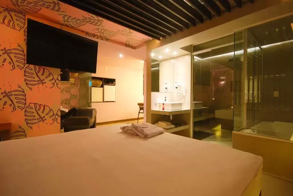 A hotel room with a bed, a TV mounted on the wall, a glass-enclosed bathroom, and a patterned wall.