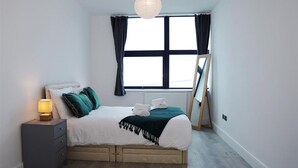 Een slaapkamer met een bed, nachtkastje, lamp, raam en een losstaand ezel.