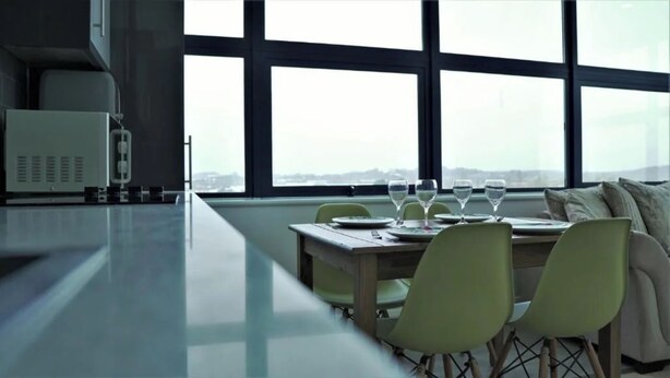 Een moderne eetruimte met een lange tafel, stoelen en uitzicht door grote ramen.