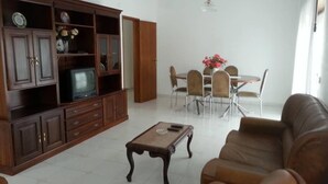 A living room with a wooden cabinet, a television, a dining table with chairs, and a leather sofa. - Apartamentos Odeceixe (Aljezur)