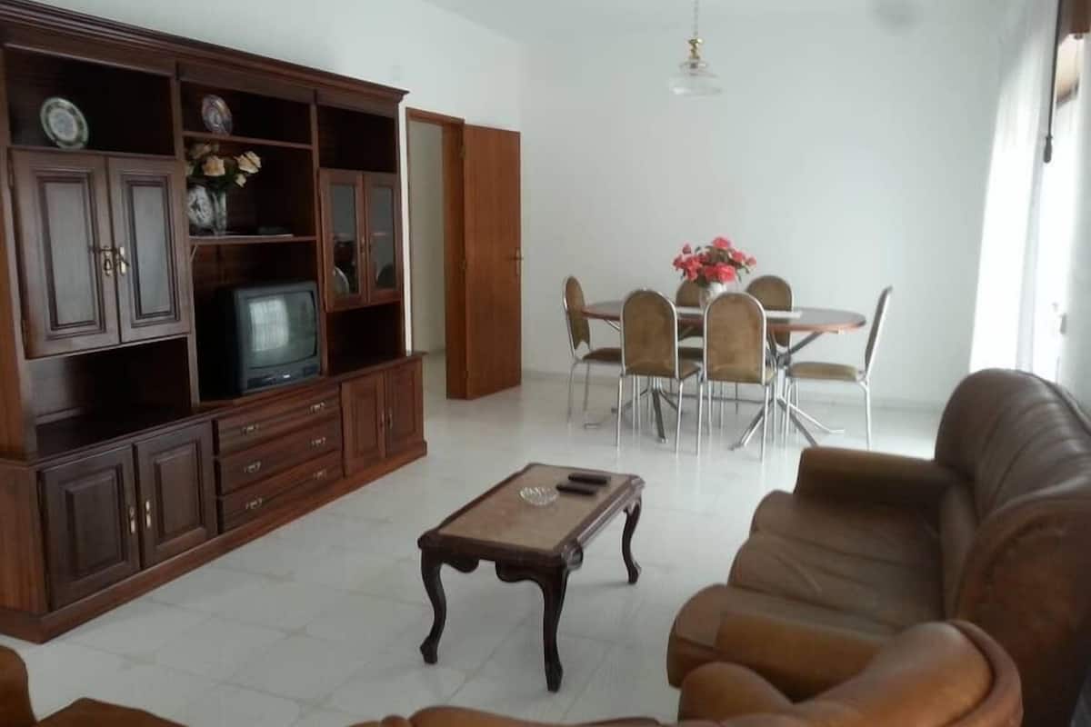 A living room with a wooden cabinet, a television, a dining table with chairs, and a leather sofa.