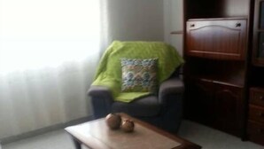 A room with a wooden coffee table, a chair with a green cover, and a bookshelf. - Apartamentos Odeceixe (Aljezur)