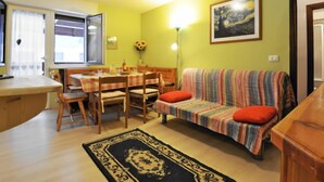 Un salon chaleureux avec un coin repas, un canapé agrémenté de coussins colorés et un tableau accroché au mur.