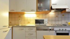 Een kleine keuken met witte kastjes, een magnetron, een fornuis en een vaatwasser.
