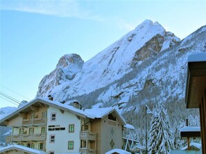 A multi-story building with balconies, a sign reading "Hotel Villa Grist," and snow-covered mountains in the background.