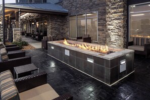 An outdoor patio with a stone fireplace, wicker furniture, and a stone wall. - TownePlace Suites by Marriott Midland South/I-20 (Midland)
