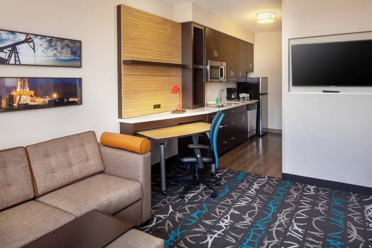 Une chambre d’hôtel moderne équipée d’un canapé, d’un bureau avec un ordinateur, d’un coin cuisine et d’un téléviseur à écran plat.