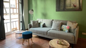 Un salon avec un mur vert, un canapé avec des coussins, une table ronde en bois, un lampadaire et une fenêtre avec des rideaux.