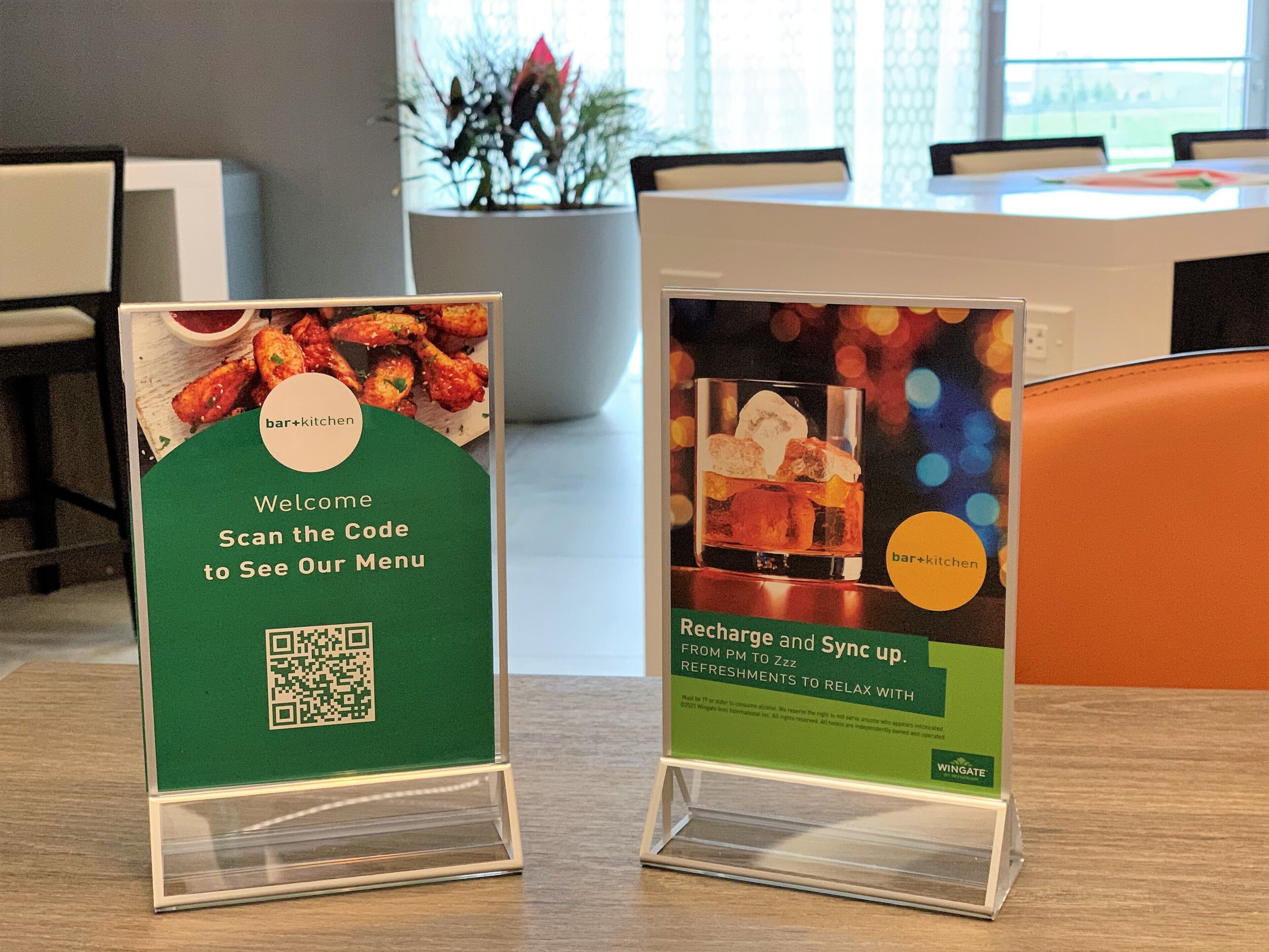 Två informationsstånd i en modern kontorsmiljö, det ena för en bar- och cateringverksamhet med en QR-kod, och det andra för en tjänst som erbjuder laddning och synkronisering.
