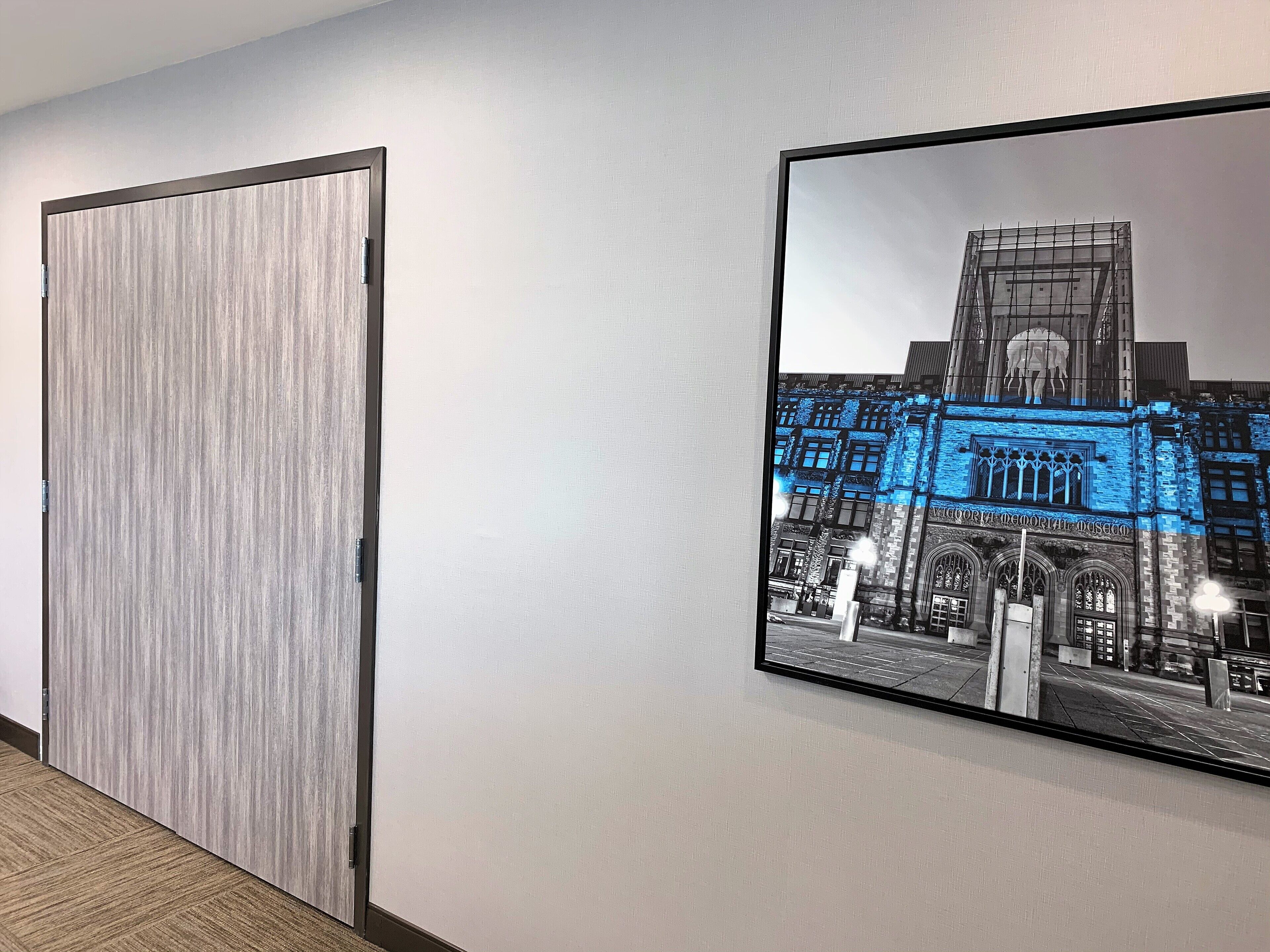 A hallway with a wooden door and a framed picture of a building with illuminated blue lights.