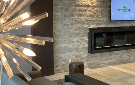 A modern interior with a stone wall, a mounted TV displaying 'Wingate by Wyndham', and a contemporary light fixture.
