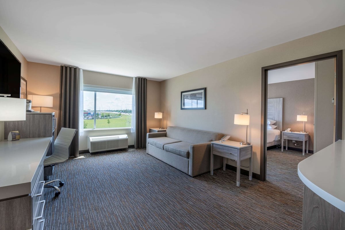 A hotel room with a large window, a sofa, a desk, and a bed.