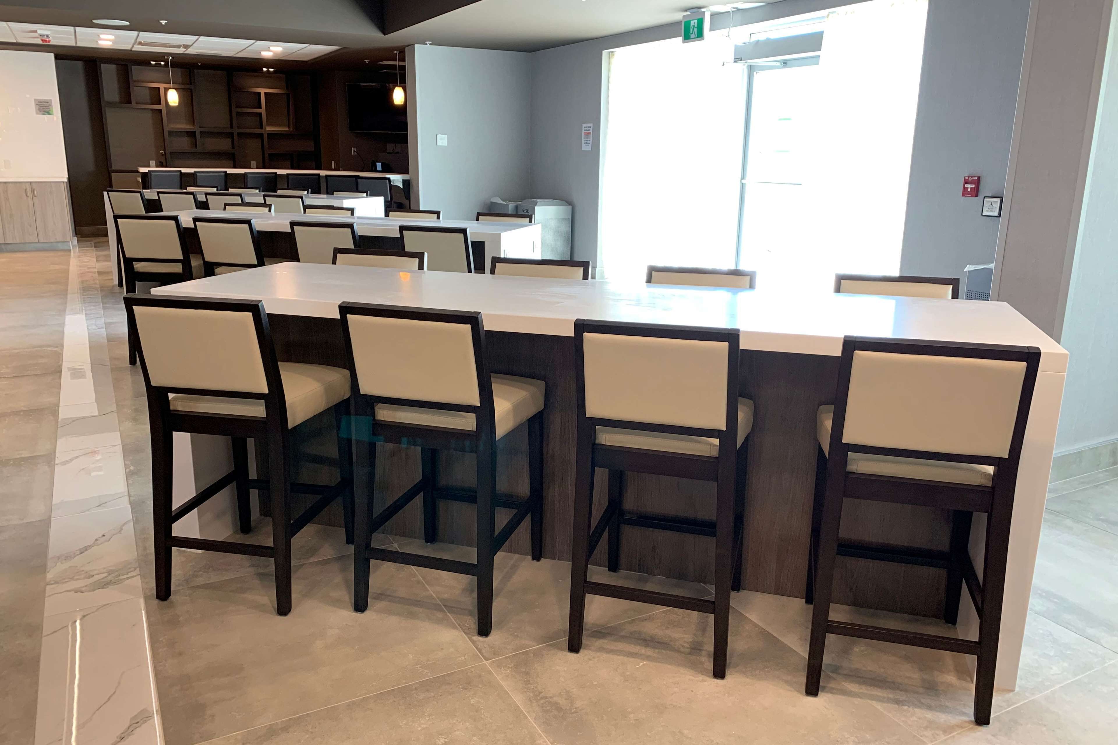 Un comedor espacioso con varias mesas y sillas, una cocina al fondo y un ventanal que proporciona luz natural.