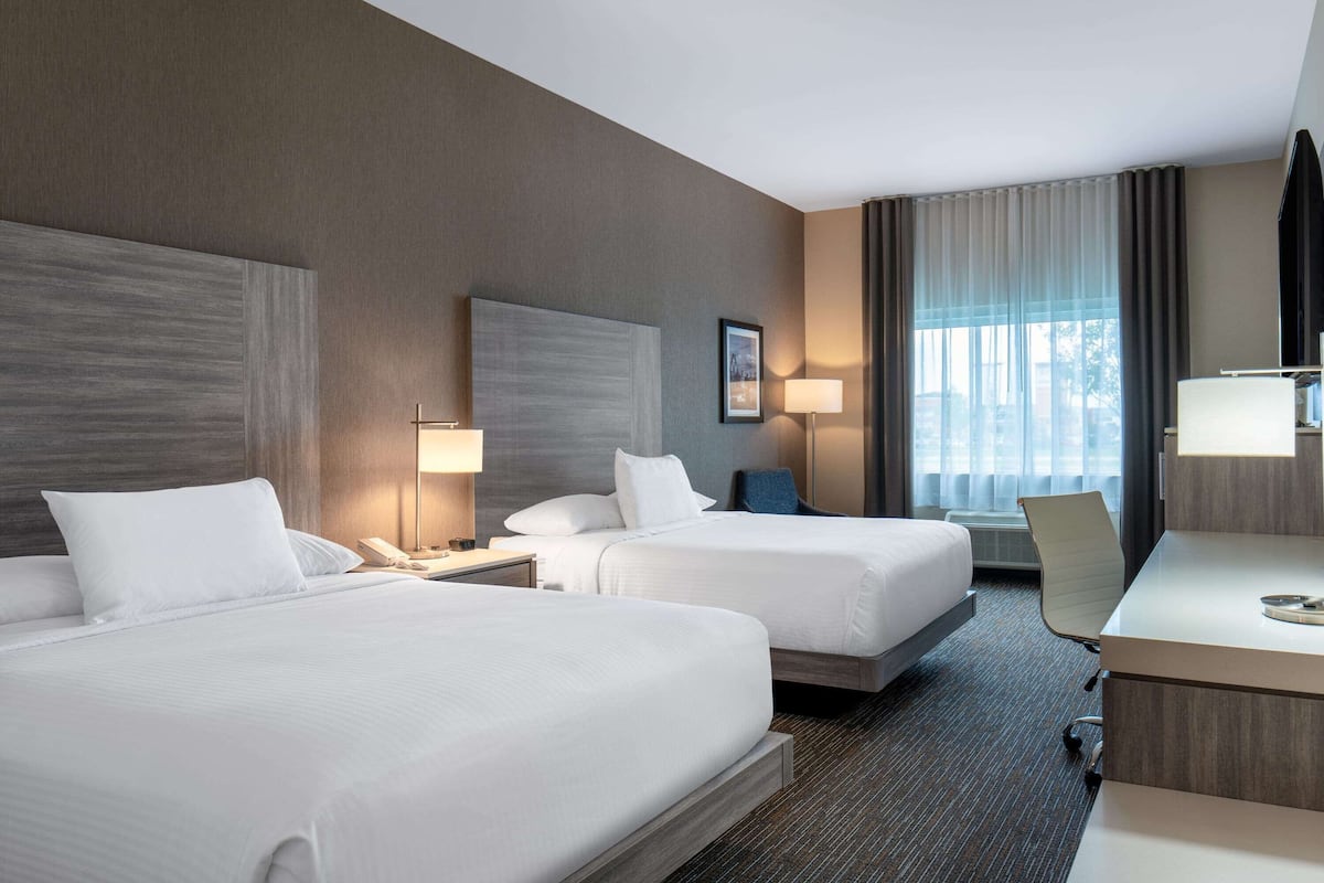 A hotel room with two beds, a desk, a chair, and a large window with curtains.