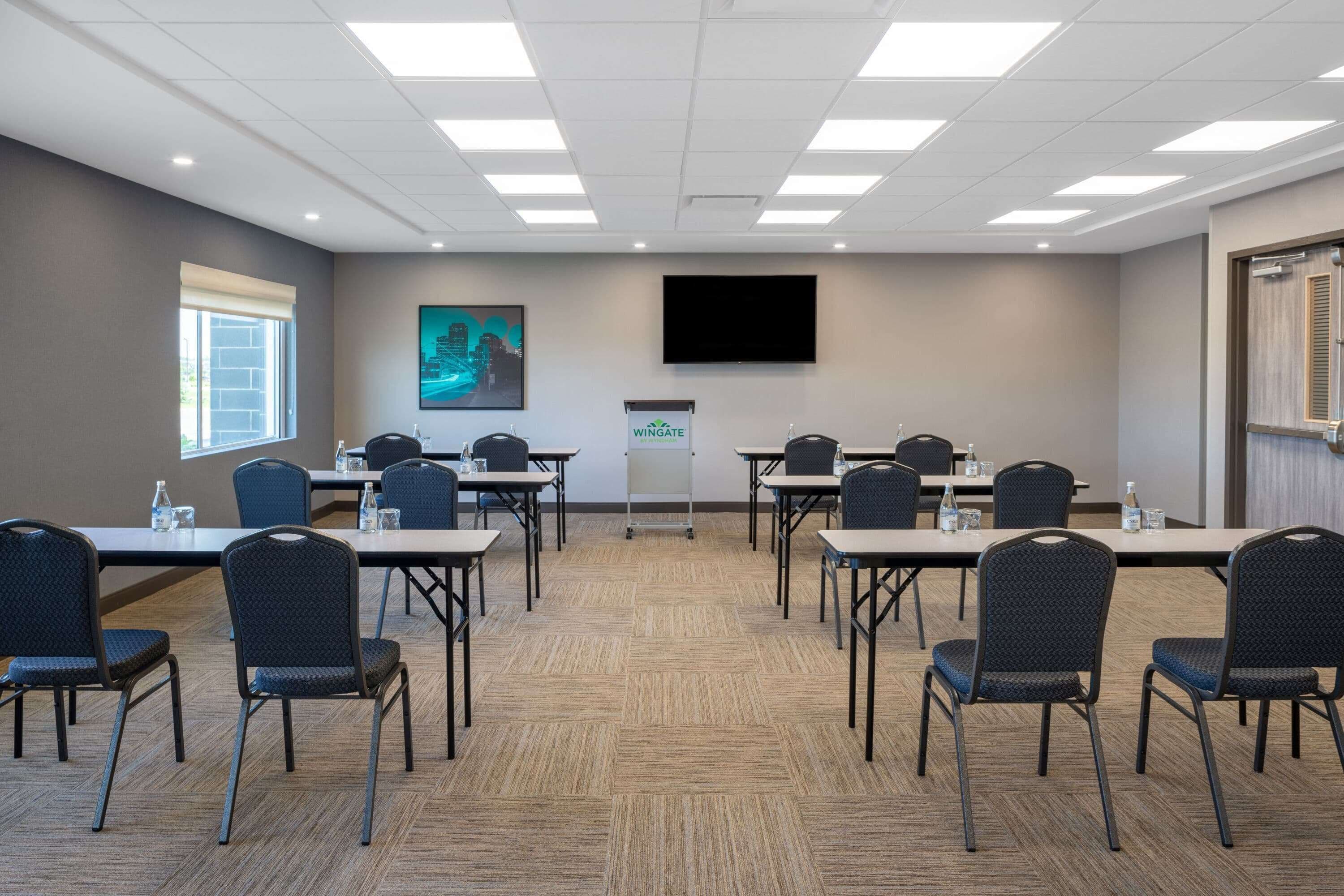 A conference room with a large screen, a podium, and multiple tables with chairs.