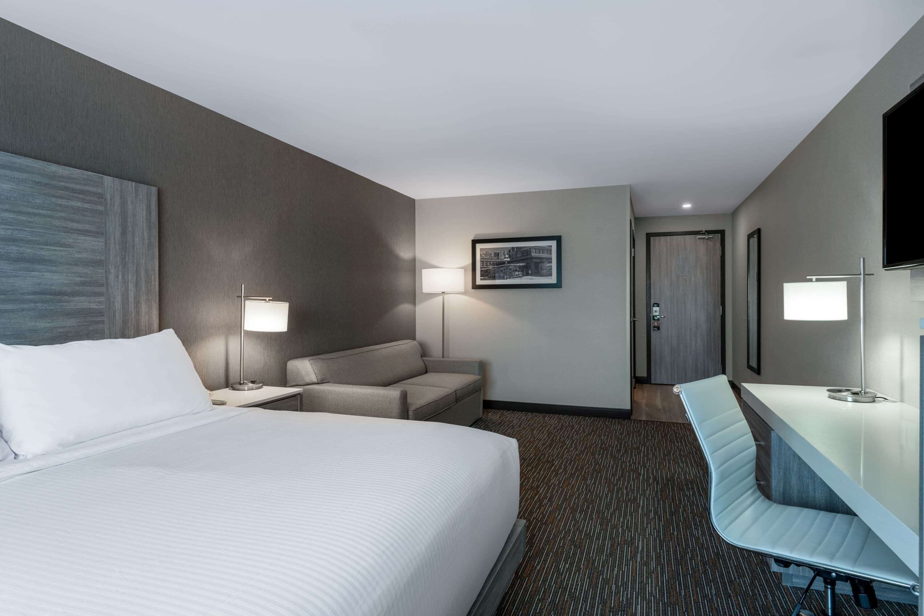 Una habitación de hotel con una cama grande, un escritorio, una silla, un sofá y un televisor.