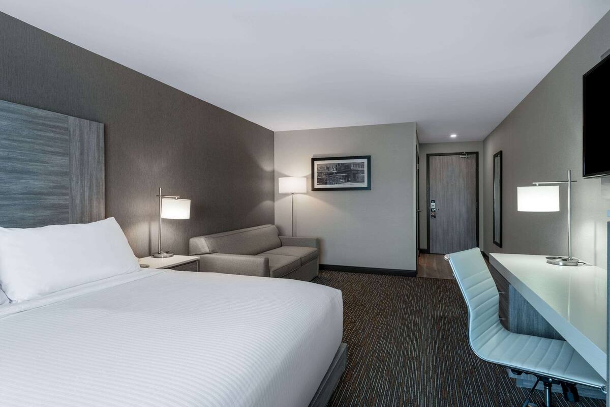 A hotel room with a large bed, a desk, a chair, a sofa, and a television.