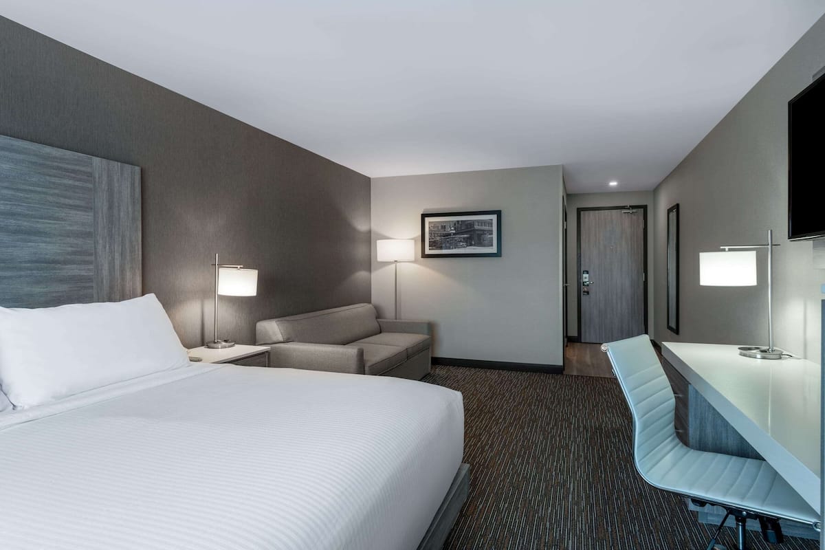 Una habitación de hotel con una cama grande, un escritorio, una silla, un sofá y un televisor.