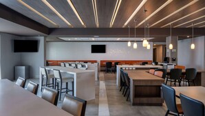 A modern dining area with multiple tables and chairs, a long counter, and pendant lighting.