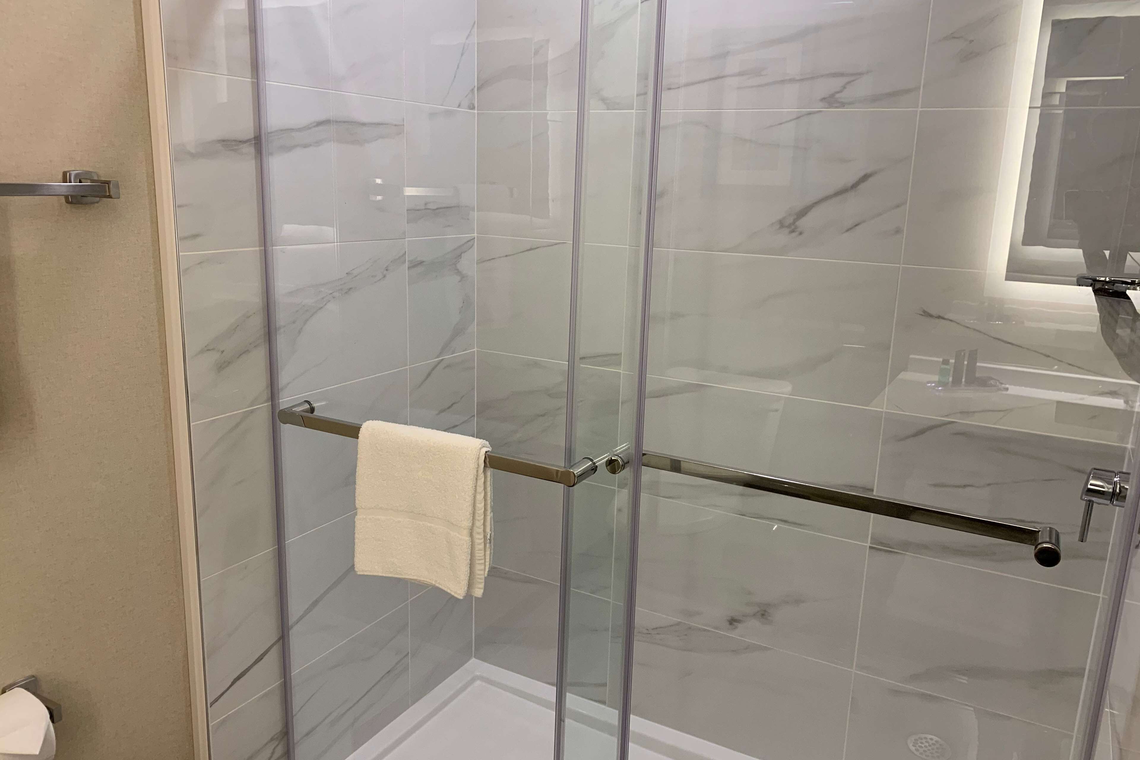 Eine gläserne Dusche mit Handtuchhalter und Wandverkleidung aus Marmor.