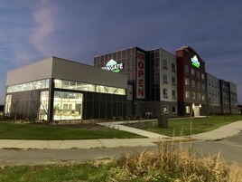 Egy modern hotel, üveg homlokzattal, feltűnő „NYITVA” felirattal és tetőterasszal.