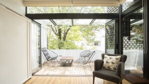 A modern patio with a wooden floor, a table, two chairs, and a sofa with a patterned cushion. - Central Luxury house - Condesa Neighborhood (Colonia Condesa)