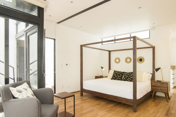 Une chambre moderne avec un lit à baldaquin, un canapé gris et une petite table.