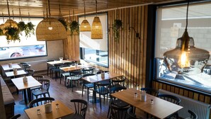 A restaurant interior with wooden walls, hanging wicker lamps, and a large window with a view of the street. - Hotel Boutique Restaurant Kran Kreen (Punta Arenas)