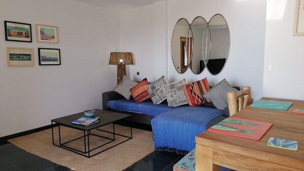 Ein modernes Wohnzimmer mit einer Couch, einem Couchtisch und einem Holzessttisch. An den Wänden hängen gerahmte Bilder und über der Couch hängt ein Spiegel.