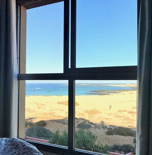 A room with a large window overlooking a beach.