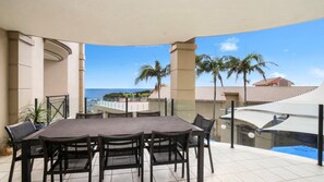 Um alpendre coberto com mesa e cadeiras, com vista para a praia e palmeiras.