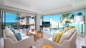 Un salón amplio con un televisor grande, asientos cómodos y vistas al océano a través de grandes ventanales.