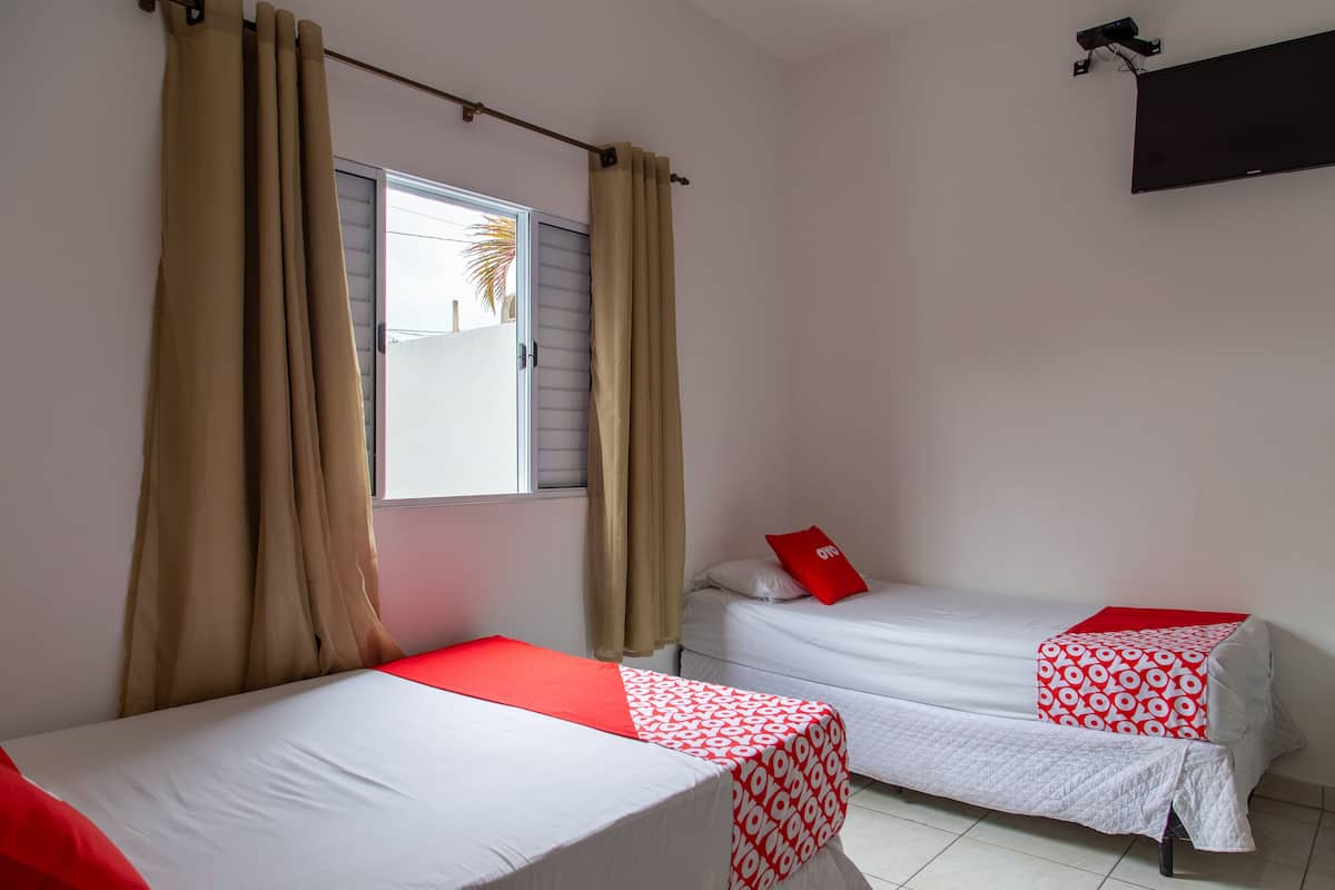 Une chambre avec deux lits, des rideaux beiges, une fenêtre et un téléviseur fixé au mur.