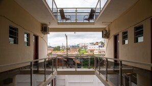 Une vue depuis un balcon doté d’une balustrade en verre, donnant sur un paysage urbain avec des bâtiments et un ciel dégagé.